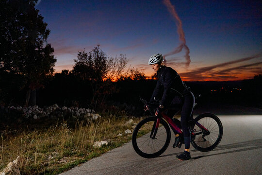 Female Cyclist Riding Road Bike at Sunset on Quiet Country Road During Evening Training