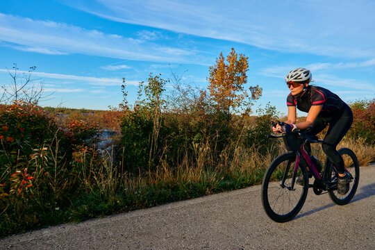 Female Cyclist Training On A Road Bike Along A Scenic Autumn Trail Under Blue Sky