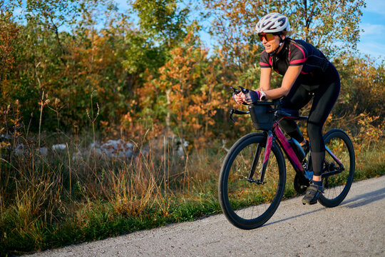 Female Cyclist Training on Road Bike in Autumn Countryside Wearing Helmet and Cycling Gear
