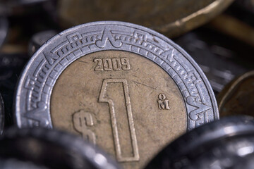 Mexican one peso coin stands upright among other coins in a pile © Omar