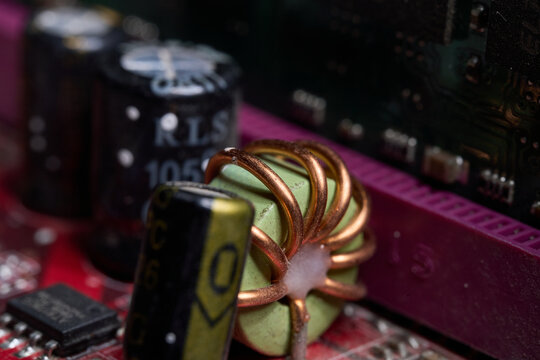 A copper coil inductor and electronic capacitors are sitting on a red printed circuit board inside a computer hardware system