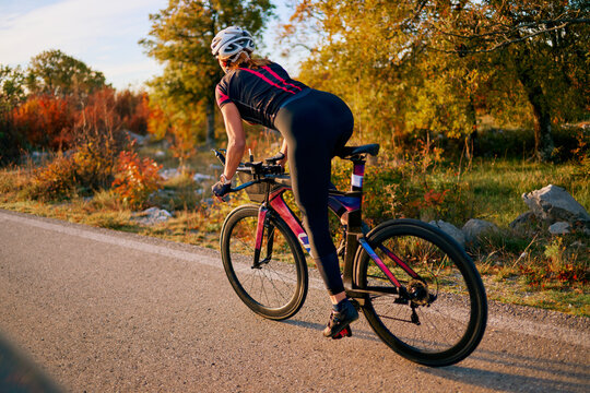 Female Cyclist Training on Road Bike Through Autumn Countryside at Sunset for Fitness