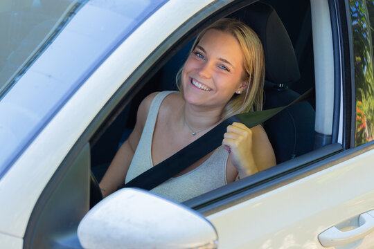 Young smiling woman fastening seatbelt while sitting in car, cheerful female driver ready for safe road trip