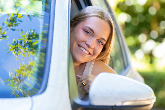 Happy young woman smiling and looking out of car window during road trip