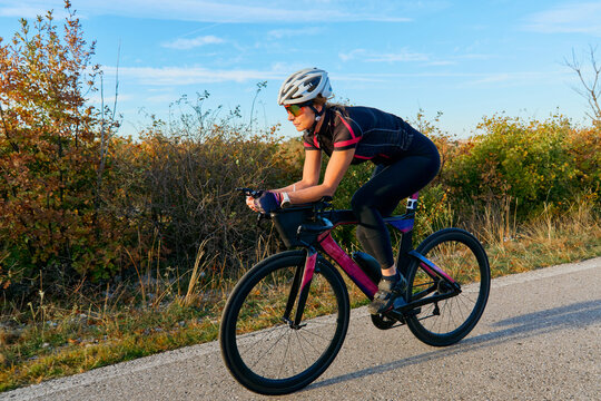 Female Cyclist Training On Aerodynamic Road Bike During Autumn Morning Countryside Ride