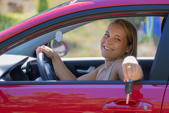 Young woman smiling and holding car keys while sitting in the driver's seat of her new car, celebrating her first vehicle purchase