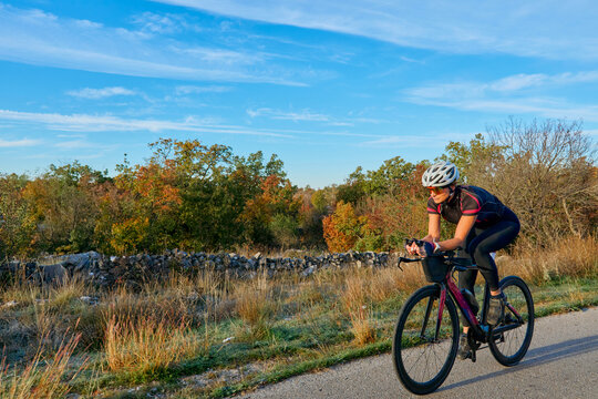 Female Cyclist Riding Road Bike Through Autumn Countryside at Sunrise for Fitness and Training
