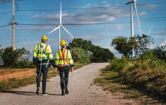 Two workers in high-visibility vests walk along a gravel path