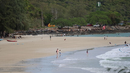 Obraz premium The image depicts a sandy beach with several people enjoying the shoreline. Some individuals are walking along the water's edge, while others appear to be playing or relaxing near the surf