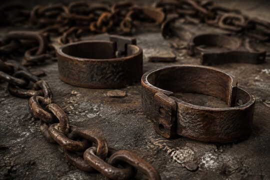 Rusty iron chains and shackles scattered on textured ground, weathered metal surfaces.