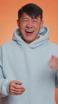 Amused Asian man pointing finger to camera, laughing out loud, taunting making fun of ridiculous appearance, funny joke anecdote. Handsome Chinese boy isolated alone on orange studio background