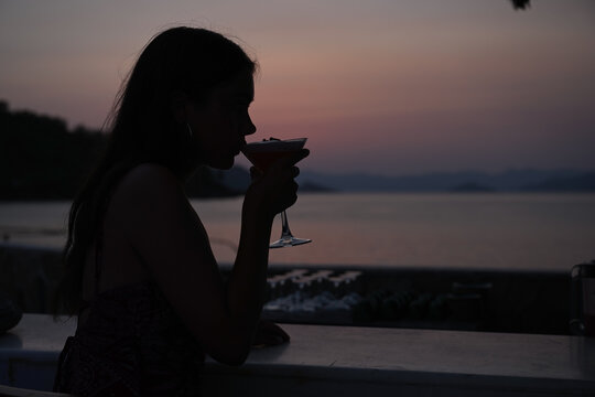 Silhouette of a young girl sipping a cocktail in an outdoor bar