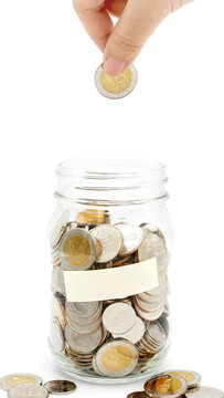 Woman's hand dropping ten Thai Baht coin into a glass jar full of coins. Business and finance concept. Vertical Photography.