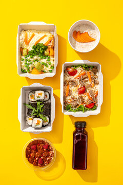 Assorted daily healthy meal ration with sushi rice dessert and beverage in takeaway boxes on yellow surface