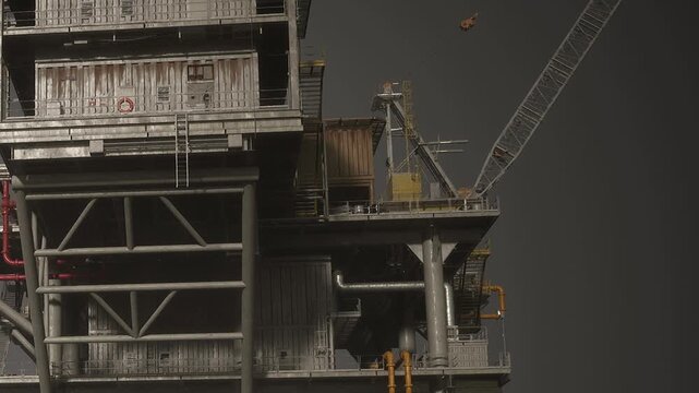 A tall oil rig structure is set in the ocean during the day. The gray sky adds to the industrial scene, with cranes and various equipment visible on the rig.