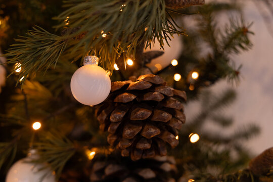 Decorative ornaments and pine cones hang from a Christmas tree in a warm setting during the holiday season