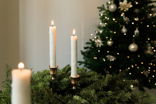 Decorative candles on green foliage with a Christmas tree in the background during a holiday gathering