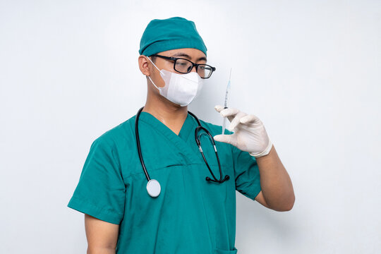 Asian male doctor in green scrubs and face mask holding syringe on white background, medical injection, flu shot, anesthesia preparation, and healthcare safety.
