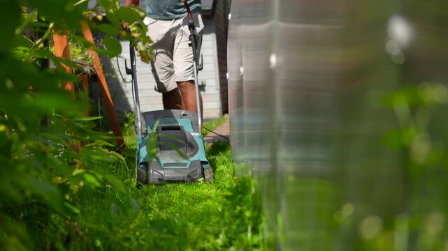 Highly engaging commercial ready low angle video of an electric lawn mower moving forward directly into the camera on a green backyard lawn.