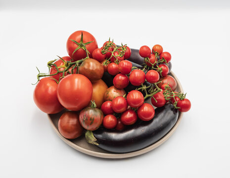 Large tomatoes, cherry tomatoes and dark eggplants form a colorful assortment of freshly picked vegetables grown in a home garden.
