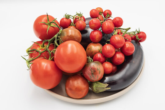 Large tomatoes, cherry tomatoes and dark eggplants form a colorful assortment of freshly picked vegetables grown in a home garden.