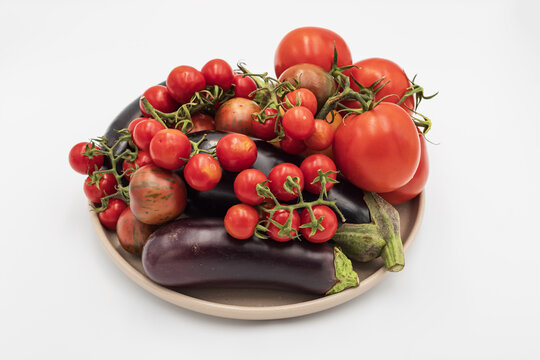 Large tomatoes, cherry tomatoes and dark eggplants form a colorful assortment of freshly picked vegetables grown in a home garden.