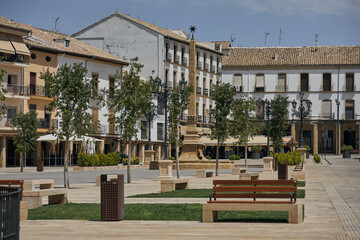 Historic public square with traditional buildings, stone monument, ornamental street lamps and tiled roofs in Baeza, Andalusia, Spain © Goodwoon Mallorca