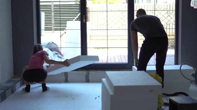 Highly engaging commercial ready video of a young couple installing styrofoam insulation panels on a kitchen floor before underfloor heating setup.