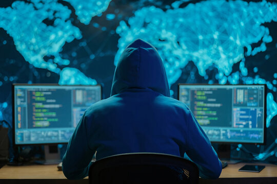 Hacker in a blue hoodie working on multiple monitors against a glowing digital world map