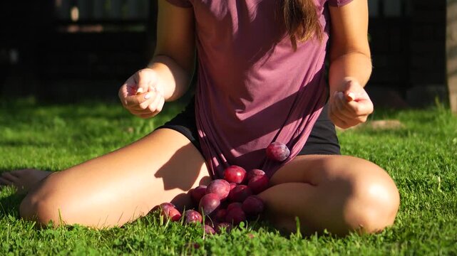 Highly engaging commercial ready slow motion video of a woman releasing her tucked shirt, letting fresh ripe plums fall out onto a green lawn.