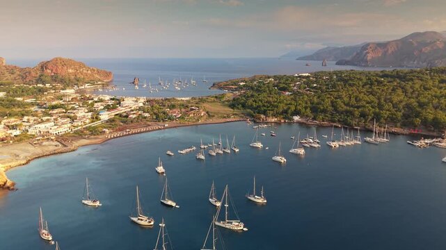 Dozens of luxury boats float peacefully in the scenic harbor of Vulcano island Sicily, Italy. Sailing yachts rest at anchor along the unique black sand shores of Vulcano island