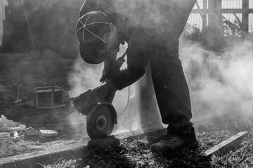 Fototapeta premium A worker builds a curb using various tools, including an angle grinder, in black and white