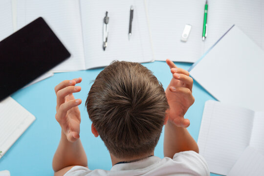 student holding head stressed with homework assignments overwhelmed young boy top view blue background with notebooks and tablet with copy space for banner design, education difficulty psychology