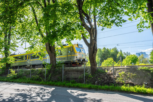 Bor?s, Sweden - May 28 2023: Electric passenger train traveling through leafy urban railway corridor.