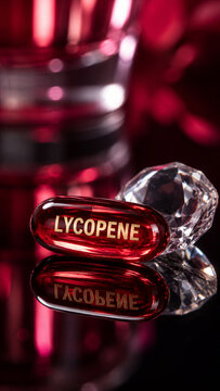 Bright red lycopene capsule rests on a smooth, reflective surface. Nearby, there are shiny gemstones and glass objects creating an interesting scene