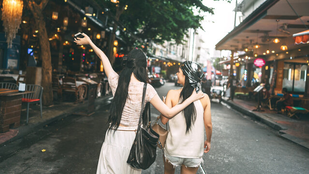 Rear view of two young asian woman hanging out with friends at Khao san walking street hipster style