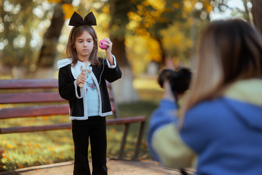 Mother Photographing Her Little Girl Playing With Kendama In Park. Loving mom captures outdoor portraits of her daughter holding a colorful toy