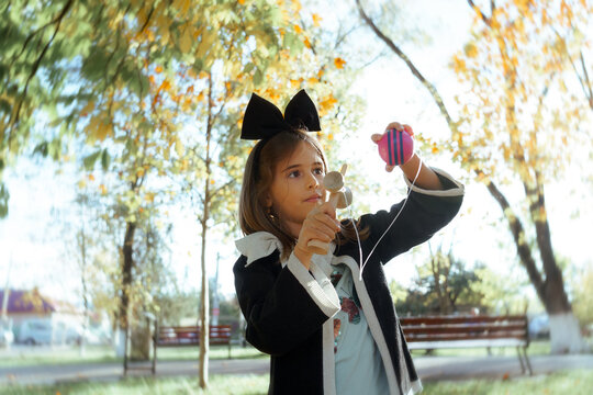 Little Girl in School Uniform Playing with Kendama Toy Outdoors. Schoolgirl with a black bow in her hair stands in an autumn park focusing on a traditional wooden toy 