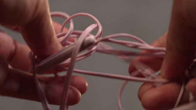 Macro close up of woman fingers untangling dense knot on wired headphones, giving up passively, barrier concept.