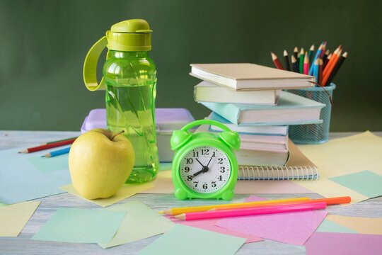 School supplies and healthy lunch on the study table. Bottle of water and lunch box and alarm clock, textbooks, colored pencils: back to school concept.