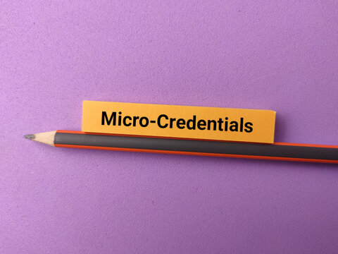 A yellow paper strip labeled Micro-Credentials rests along the side of a black and red pencil on purple