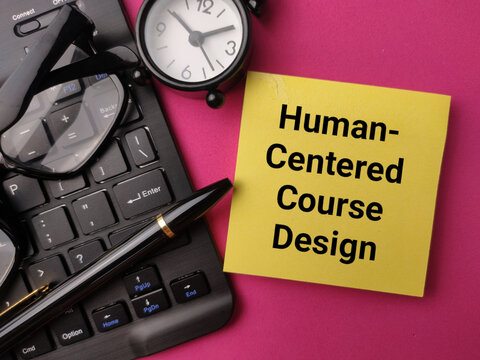 A yellow note displaying Human-Centered Course Design lies near glasses, a keyboard, clock, and pen on pink