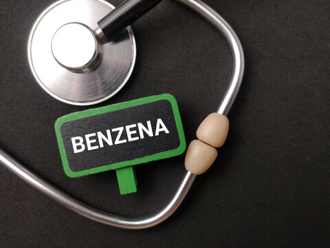A green wooden clip labeled BENZENA sits framed inside the loop of a stethoscope on black