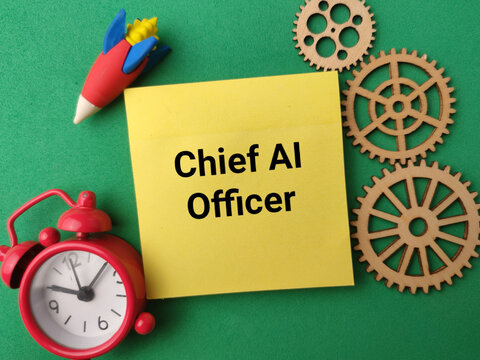 A yellow note reading Chief AI Officer rests on green beside wooden gears, a rocket, and an alarm clock