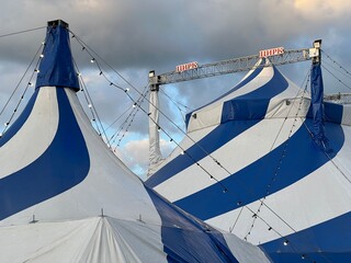 A blue and white circus tent against a cloudy sky. The inscription "Circus" in Russian © Olga