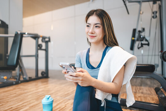 Young adult asian woman, wear sportswear using cell phone for ai health tracking app at indoor gym