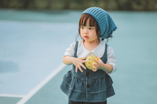Toddler girl holding ball on outdoor court, playful childhood activity and early physical development