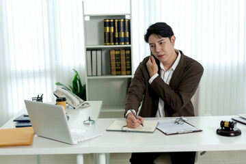 Fototapeta premium Asian Male Lawyer Writing Notes During Phone Consultation at Modern Law Office