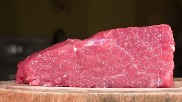 Camera dolly moving past whole piece of fresh raw beef meat on round wooden chopping board.