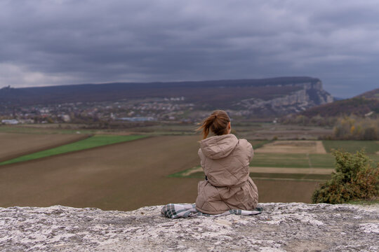 Autumn landscape panorama featuring woman sitting on cliff edge observing cloudy valley view